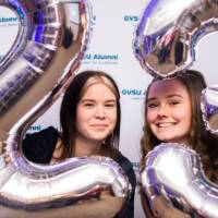 Two grads peek through the 2023 balloons for a photo